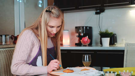 Cheerful woman practicing in gingerbreads decorating in the kitchen at home. Family culinary and traditions concept.の写真素材