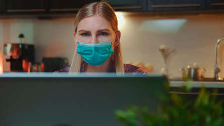 Front view of computer monitor and business woman in medical mask reading something on it. She working at home on quarantine.の写真素材