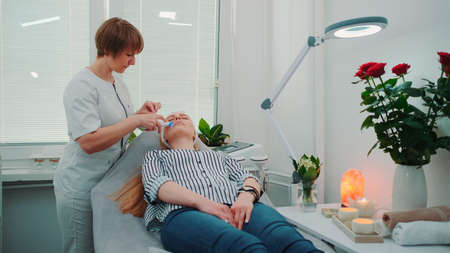 Professional cosmetologist making cavitation peeling on young womans face at beauty salon with modern equipment and pleasant atmosphere.の写真素材