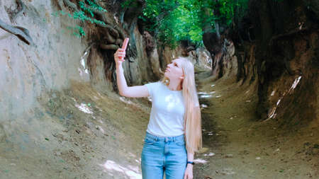 Blonde young woman making photos on smartphone in magical Roots Gorge situated in Kazimierz Dolny in Polandの写真素材