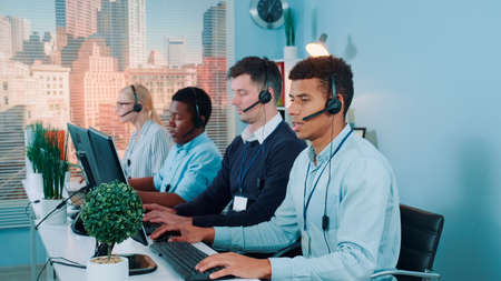 Multiracial call center agents talking to the clients in headset. There are skyscrapers in the background.の写真素材