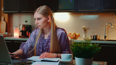Young business woman working at home by sitting at the computer. She is in home bathrobe in the kitchen.の写真素材