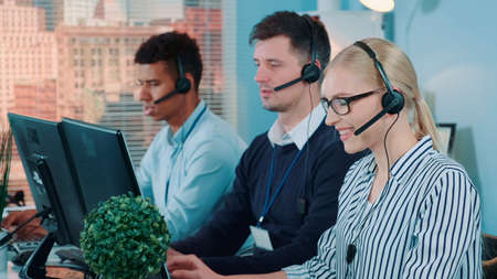 Medium shot of female customer service working in busy call center by talking to the international client. Her mixed-race team also taking calls.の写真素材
