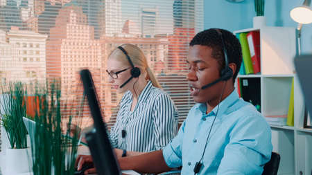 Medium shot of friendly african man working in call center. He answering international call in a headset.の写真素材
