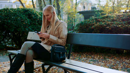 Girl communicates in a smartphone in a city park on a bench.の写真素材