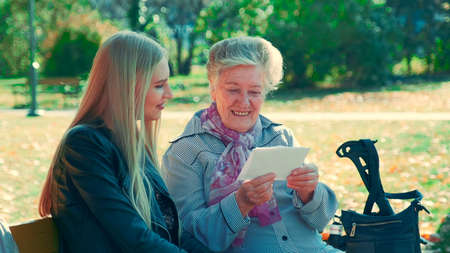 Middle close up shot of old woman reading a letter to pretty young woman in park. She reading some interesting story of her life.の写真素材