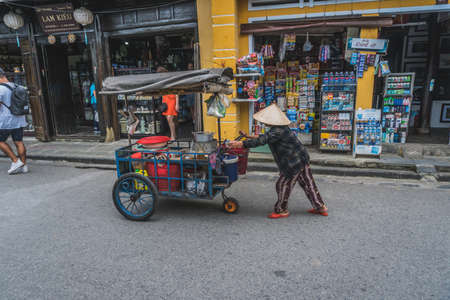 Wonderful view of old street decorated with colorful silk lanterns. Vietnamese people in traditional closes walking along Hoi An Ancient Town. Hoi An (Hoi an), Vietnam - March 12, 2020.のeditorial素材