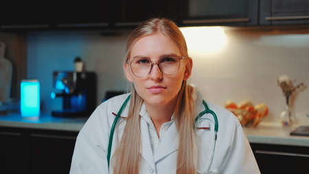 Close-up of female doctor looking to the camera and making video call to patient. She working in the kitchen at home.の写真素材