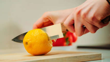 Hands with knife cutting lemon on the kitchen board. Close up shotの写真素材