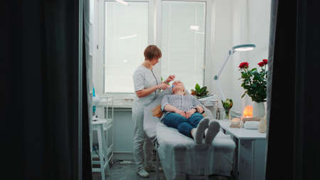 Luxury beauty salon: cosmetician making cavitation facial peeling. Woman resting after hard working week.の写真素材