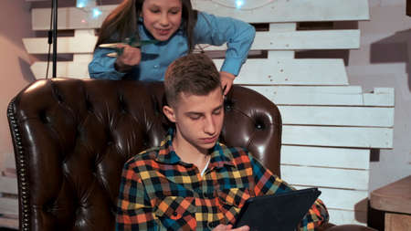 Close-up of brother hiding the tablet screen from his small sister. There is a fireplace in their living room at home.の写真素材