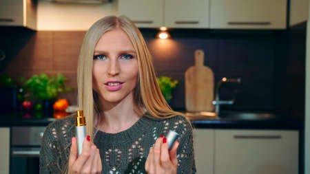 Young vlogger smelling perfume. Beautiful young woman spraying and smelling nice perfume while shooting video for beauty vlog at home.の写真素材