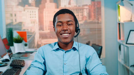 Portrait of black customer service operator in a headset smiling to the camera. There are skyscrapers in the background.の写真素材