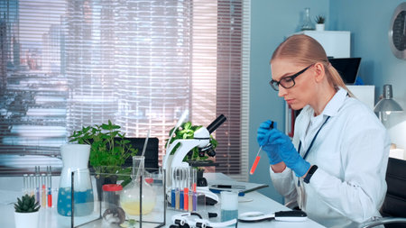 In modern research laboratory: female scientist using pipette to drop sample on slide and looking into microscope. There are different instruments and lab hamster on her table.の写真素材