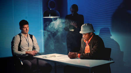 Suspected mixed-race man signing a document of accusation. Interrogation room in smoke.の写真素材