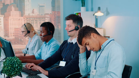 Multiracial call center agent feeling exhausted and broken-down after telephone call with the client. He working with mixed-race team in modern office.の写真素材