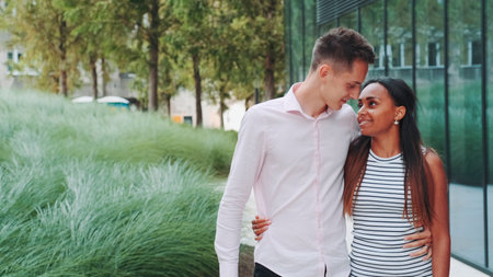 Tall young man kissing her african girlfriend while walking down the street. She telling him about something. Relationship conceptの写真素材