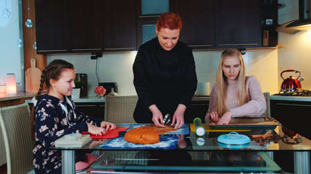 Women baking gingerbread cookies in the kitchen at home. Young girl helping them and observing the process.の写真素材