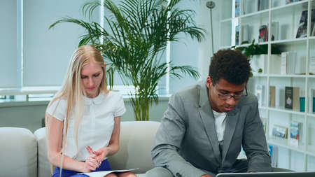 African-American man surfing laptop and sharing great news with coworkers sitting together in office around table.の写真素材
