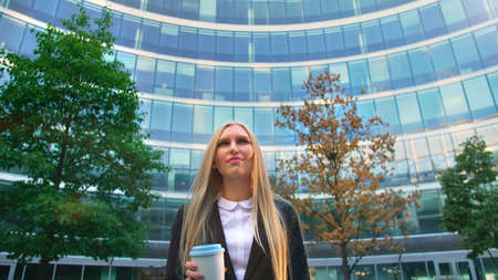 From below of serious blond executive woman in suit having coffee in paper cup looking away on street.の写真素材