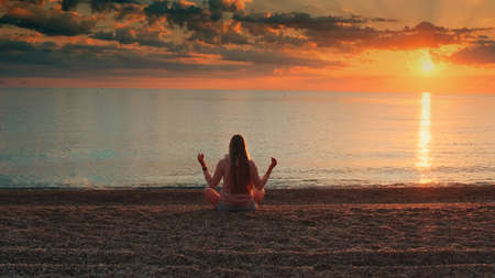Full shot of woman meditating on the seashore. Back viewの写真素材