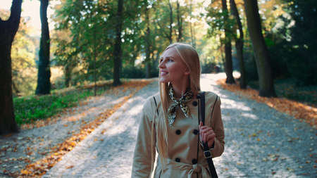 Beautiful young blonde girl walking in the park in autumn and smilingの写真素材