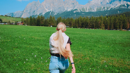 Back view of woman running on the field with mountains in front. Beautiful nature around.の写真素材