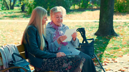 Full shot of old woman reading a letter to pretty young woman in park. She reading some interesting story of her life.の写真素材