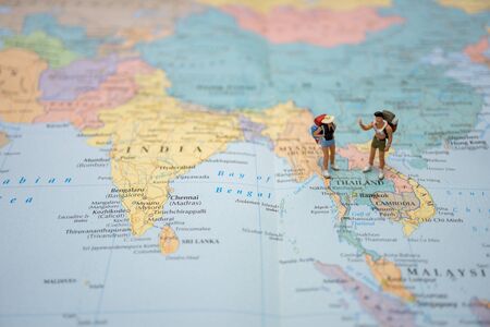 A little figure couple backpacker or miniature couple tourist male and female stand and walk on map...