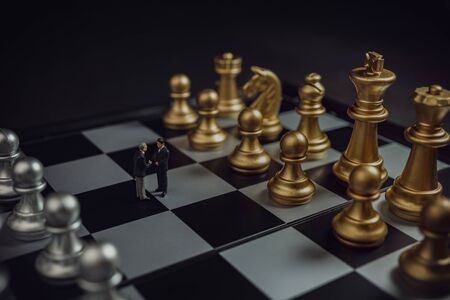 Miniature business partnership handshake concept. Successful businessmen handshaking after good deal on gold and silver chess background.の写真素材