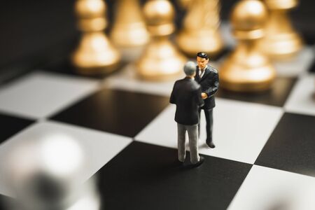 Miniature business partnership handshake concept. Successful businessmen handshaking after good deal on gold and silver chess background.の写真素材