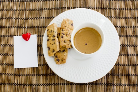 a cup of white coffee and chocolate chip cookies with notepad and smile magnet over a wooden table の写真素材