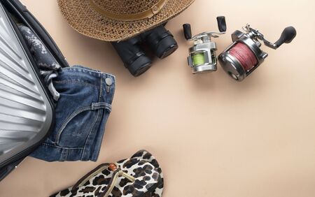 Flat lay  suitcase with binoculars, hat, jeans, spinning for fishing and saddles on pastelの写真素材