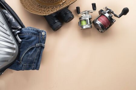 Flat lay  suitcase with binoculars, hat, jeans, spinning for fishing and saddles on pastelの写真素材