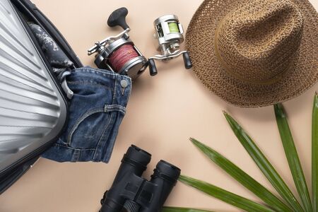 Flat lay  suitcase with binoculars, hat, jeans, spinning for fishing and saddles on pastelの写真素材