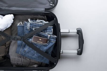 Open suitcase packed for travelling with Thailand passport on grey background - travel concept -...