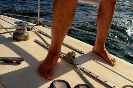 Cropped view of man legs just after bathing in the sea, standing athing on deck of pleasure yacht on the water backgroundの写真素材