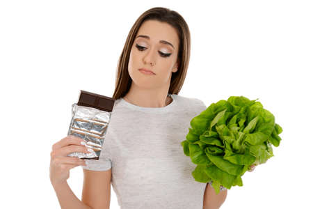 Beautiful girl holding lettuce and chocolate, looking at chocolate isolated on white backgroundの写真素材