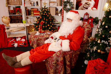Santa Claus in his house next to the fireplace and Christmas tree resting in armchairの写真素材