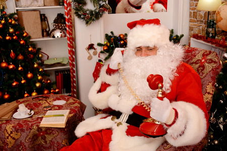 Santa Claus sitting in his wooden house in a comfortable chair and calling by vintage phoneの写真素材