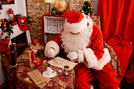 Santa Claus preparing for travel and looking at the world map. He is at home, decorated for Christmas.の写真素材