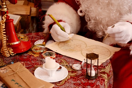 Santa Claus preparing for travel and looking at the world map. He is at home, decorated for Christmas.の写真素材