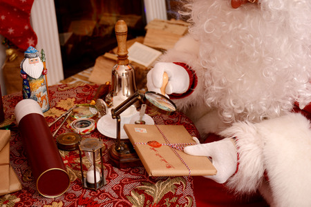 Santa Claus sealing a letter, looking through magnifier glass. Santa Claus sitting in his living room.の写真素材