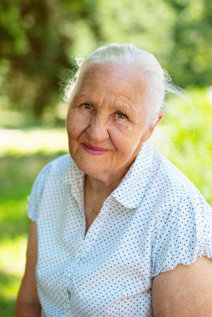 Elderly lovely woman sitting in a park, sunny summer dayの写真素材