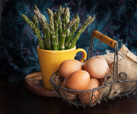 Bunch of fresh asparagus in a cup, fresh eggs on wooden tableの写真素材