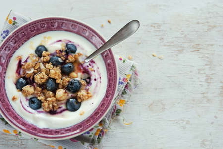 A bowl of yogurt with blueberries, cereals, granola topped with honey on a wooden white table, healthy breakfastの写真素材