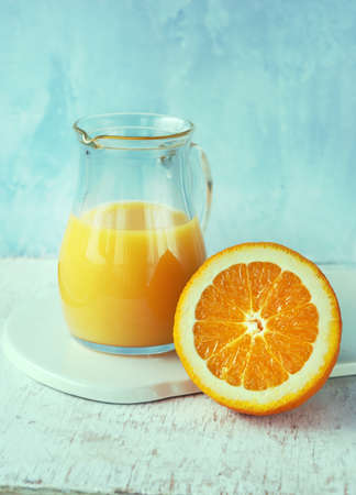 Orange juice in a pitcher and slice of orange on blue background, fresh fruits on wooden backgroundの写真素材