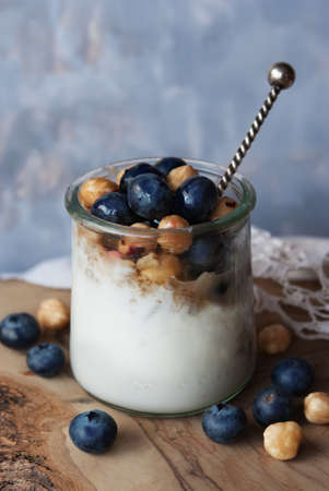 A glass of yogurt with blueberries, granola and nuts on a wooden table, healthy breakfastの写真素材