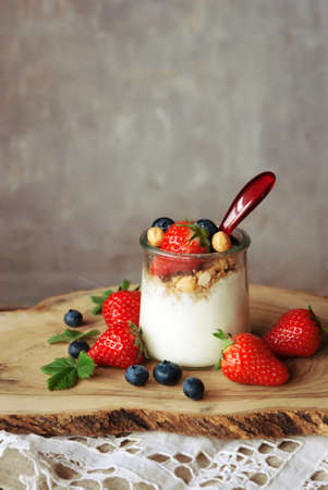 A glass of yogurt with blueberries and strawberries, granola and nuts on a wooden table, healthy breakfastの写真素材
