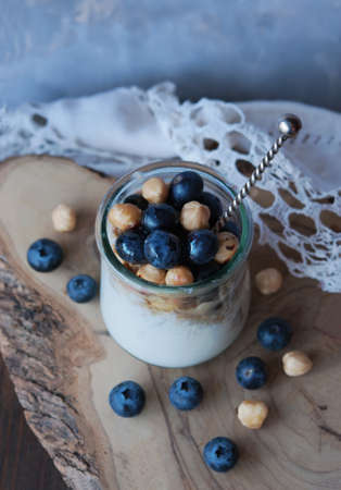 A glass of yogurt with blueberries, granola and nuts on a wooden table, healthy breakfastの写真素材